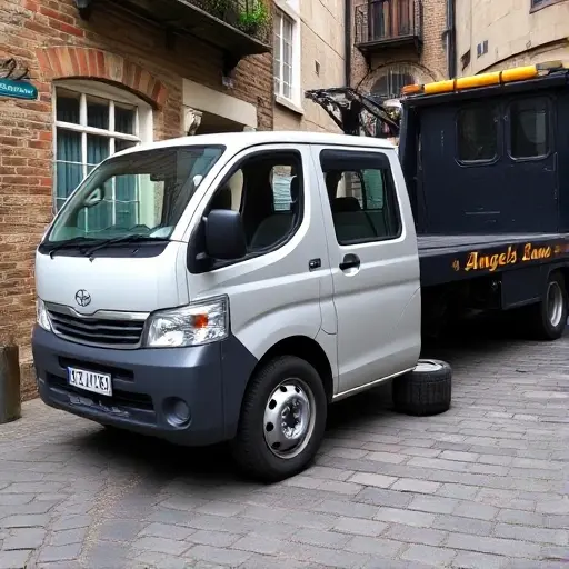 A tow truck parked on a narrow cobblestone street named Angel's Lane, with a small, broken-down car in front. The car has a flat tire, a broken side mirror, and a visible engine block. The tow truck is ready to lift the car, illustrating typical reasons for calling a tow truck such as a flat tire and engine failure.